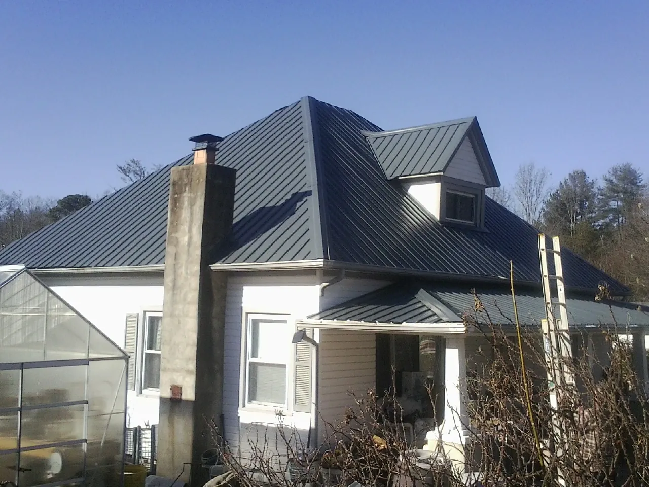 Dark blue standing seam metal roof on a white farmhouse with dormer — Slate & Tile Roof Repair by Roofing Brothers in Connellsville