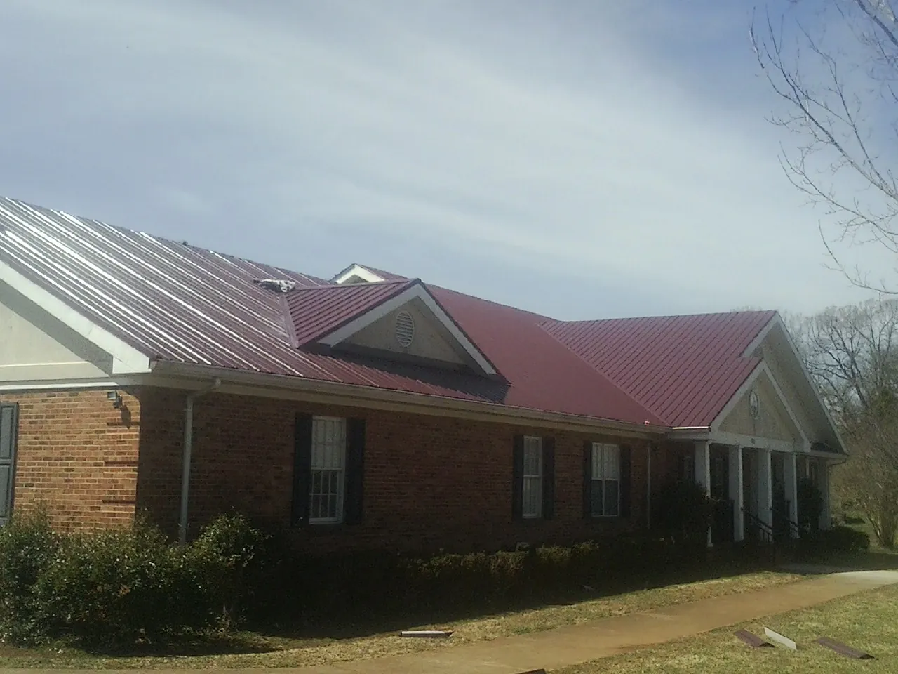 Red metal roof with gabled entries on a long brick building, from a Hail Damage Roof Repair job in Connellsville