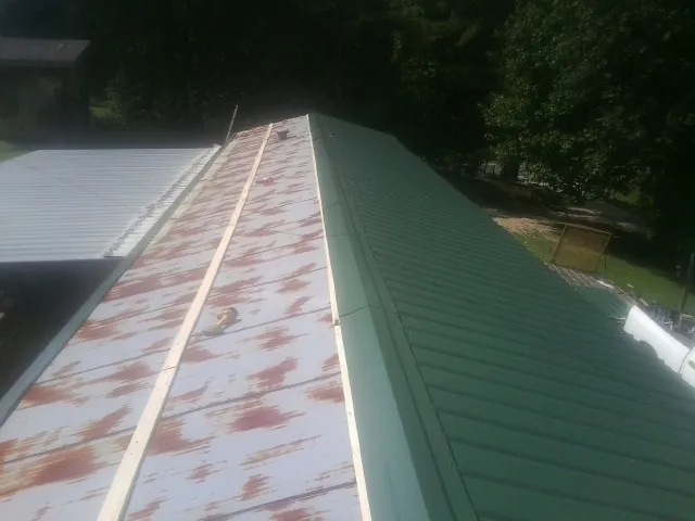 Old rusted panels beside newly installed green metal roofing — Wind Damage Roof Repair by Roofing Brothers in Connellsville