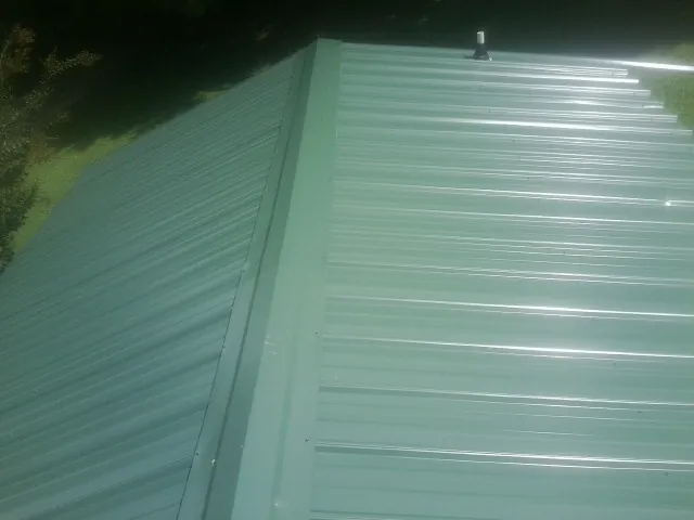 New green metal panels meeting at the ridge of a roof — Flat Roof Repair work by our crew in Connellsville