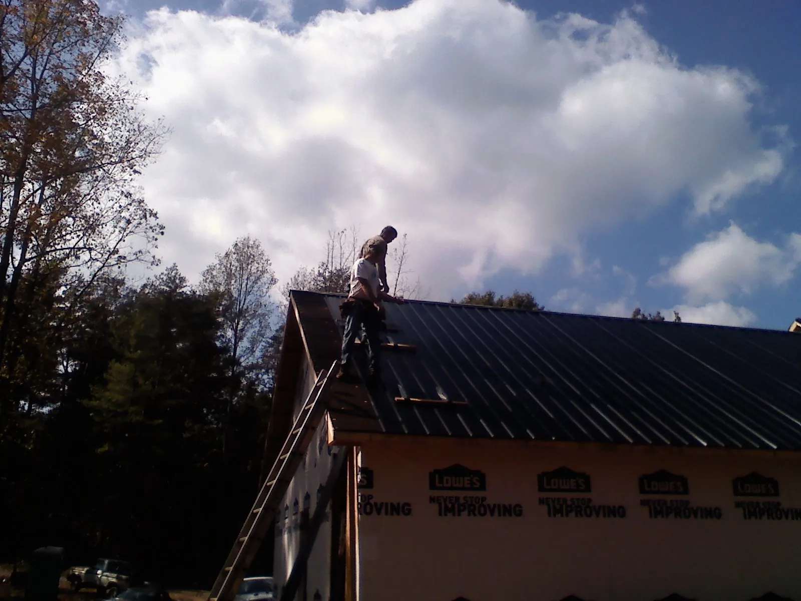 Roofer fastening dark metal panels high against a cloudy sky, from a Roof Inspection job in Connellsville