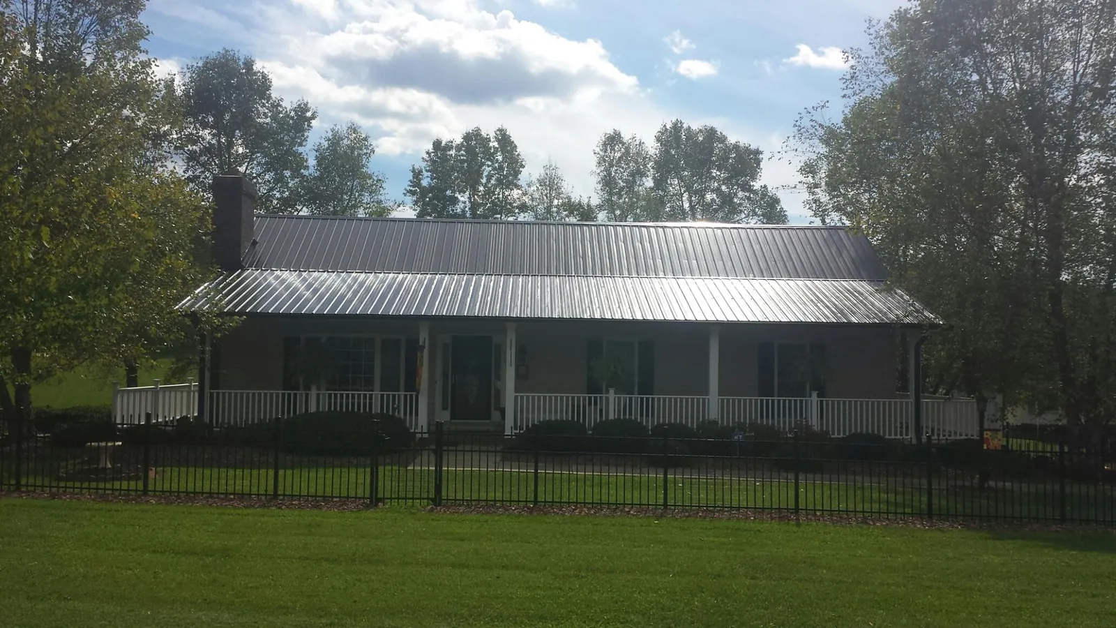Gray metal roof on a brick ranch with a full width front porch — Gutter Guard Installation work by our crew in Connellsville