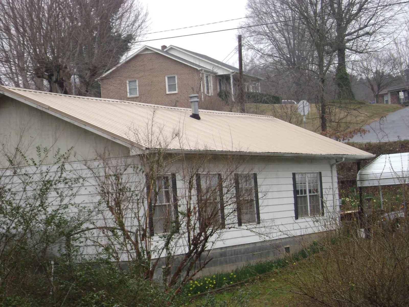 Tan metal roof on a white sided house set into a hillside — Commercial Roofing by Roofing Brothers in Connellsville